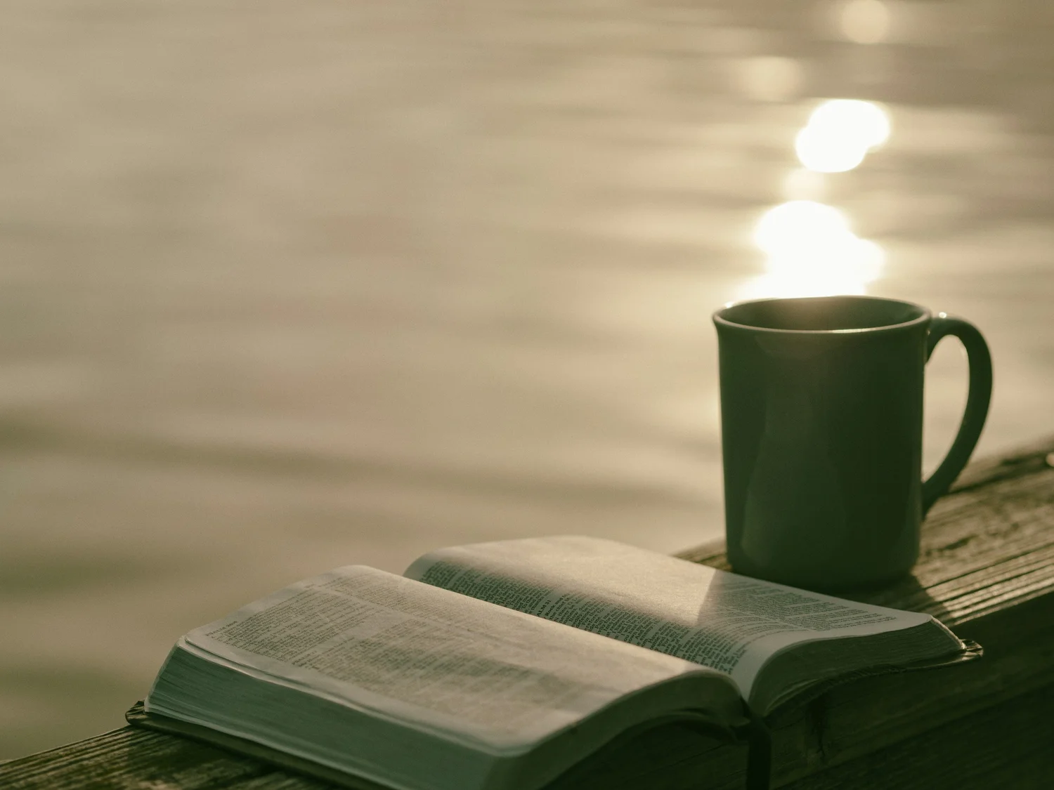 An open Bible and mug beside the water