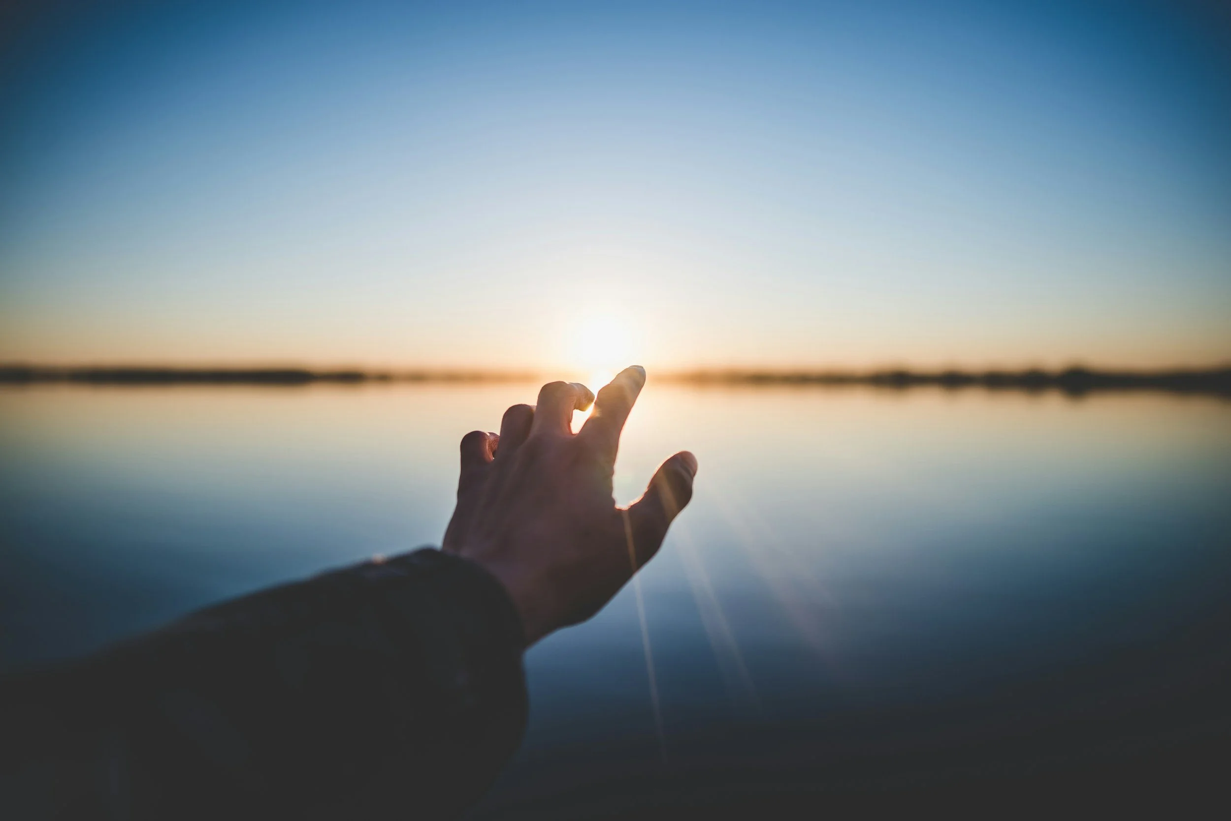 A hand reaching toward sunlight over calm water